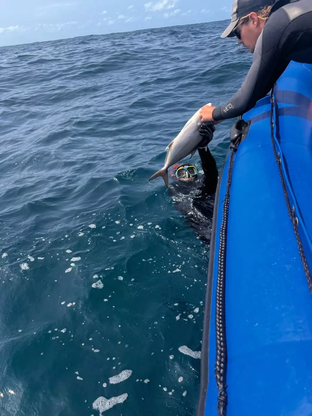 Spearfisher handing caught fish to person on boat